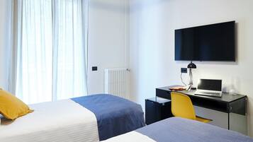 Ett hotellrum med två sängar, ett skrivbord med en bärbar dator, en stol, en tv och ett fönster med gardiner.