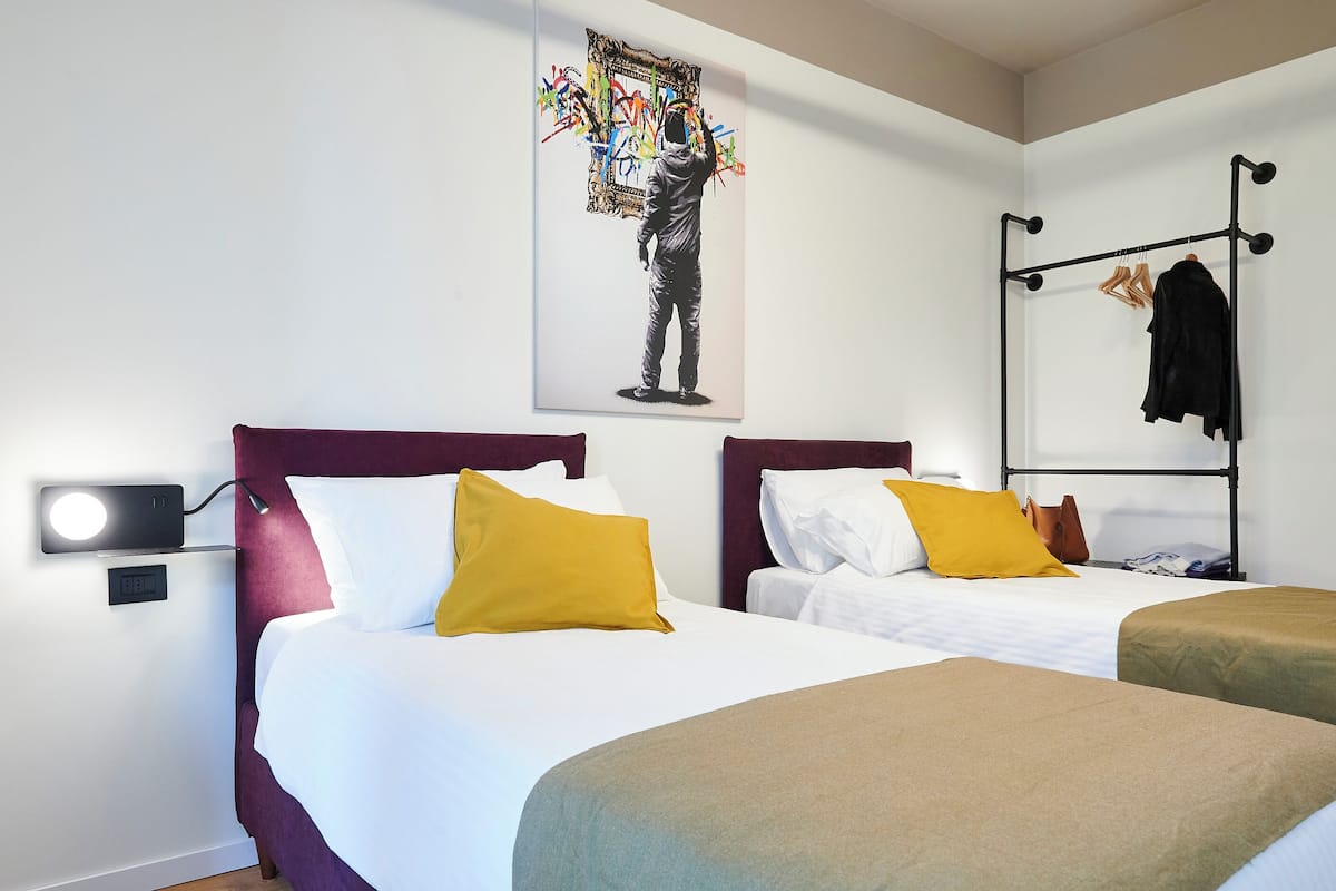 A hotel room with two beds, a wall-mounted TV, a coat rack, and a painting.