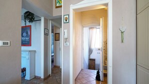 A hallway with a tiled floor, a white door, and a small plant. There is a poster on the wall and a light switch. - Elle Home: comfort in Bologna (Bologna)