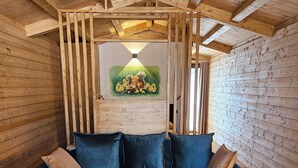 A cozy room with a wooden ceiling, a blue sofa with cushions, and a painting of a squirrel and daffodils on the wall. - La Casetta dello Scoiattolo  (Gavorrano)