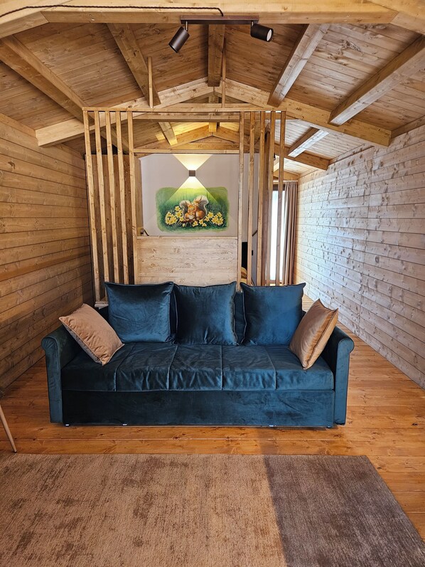 Une pièce chaleureuse avec un plafond en bois, un canapé bleu agrémenté de coussins et un tableau représentant un écureuil et des jonquilles accroché au mur.