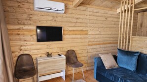A log cabin interior with a wooden wall, a mounted TV, a sofa, and a small desk with a chair. - La Casetta dello Scoiattolo  (Gavorrano)