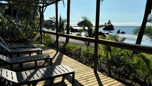 A wooden deck with lounge chairs overlooking a beach with palm trees and rocky outcrops. - JENENÉ LODGE (Nuquí)