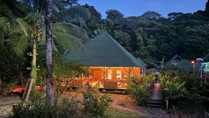 A two-story building with a green roof, surrounded by lush greenery and a paved pathway leading to the entrance. - JENENÉ LODGE (Nuquí)