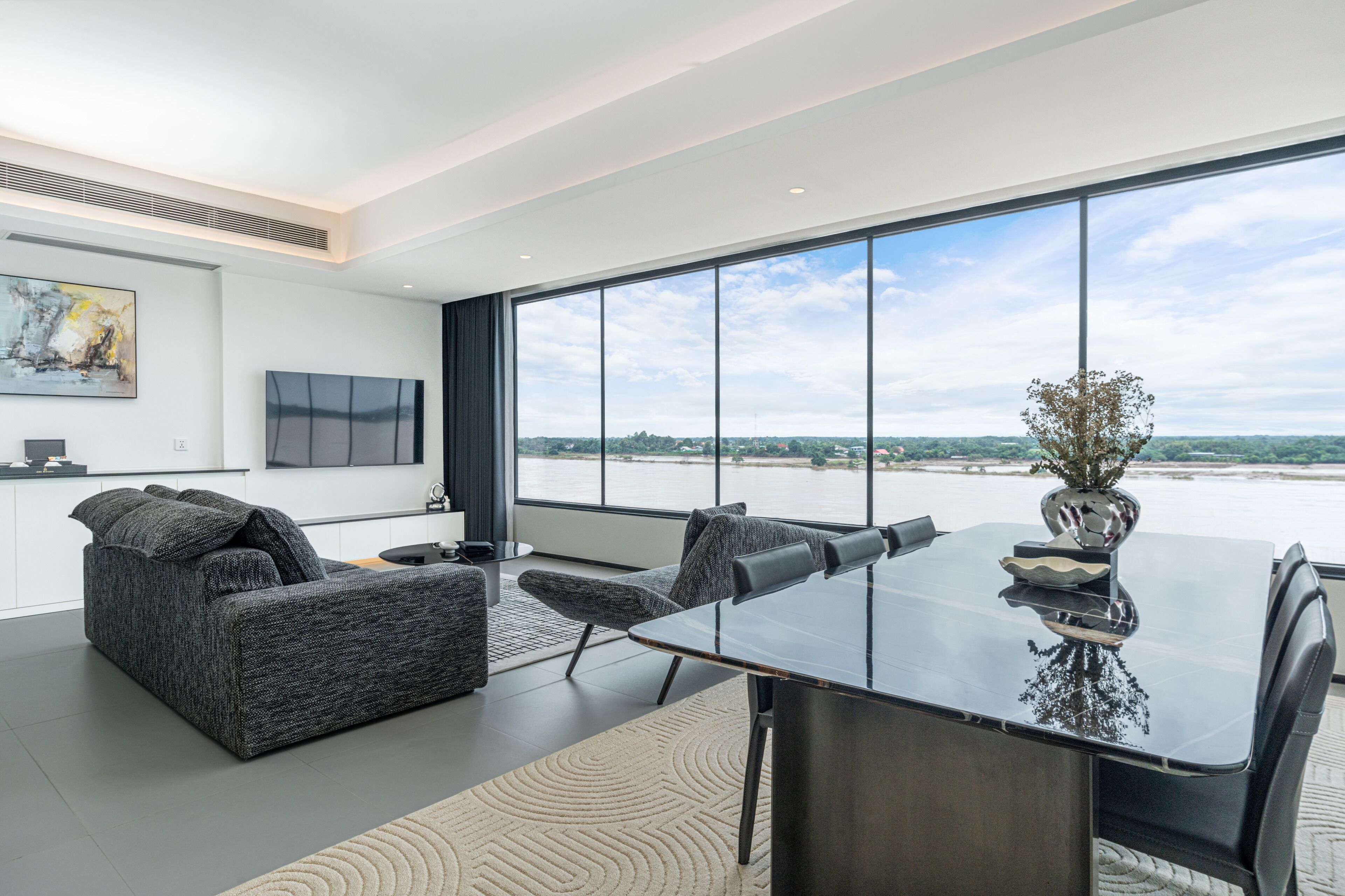 A modern living room with a large window, a sofa, a dining table, and a TV.
