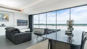 A modern living room with a large window, a sofa, a dining table, and a TV.