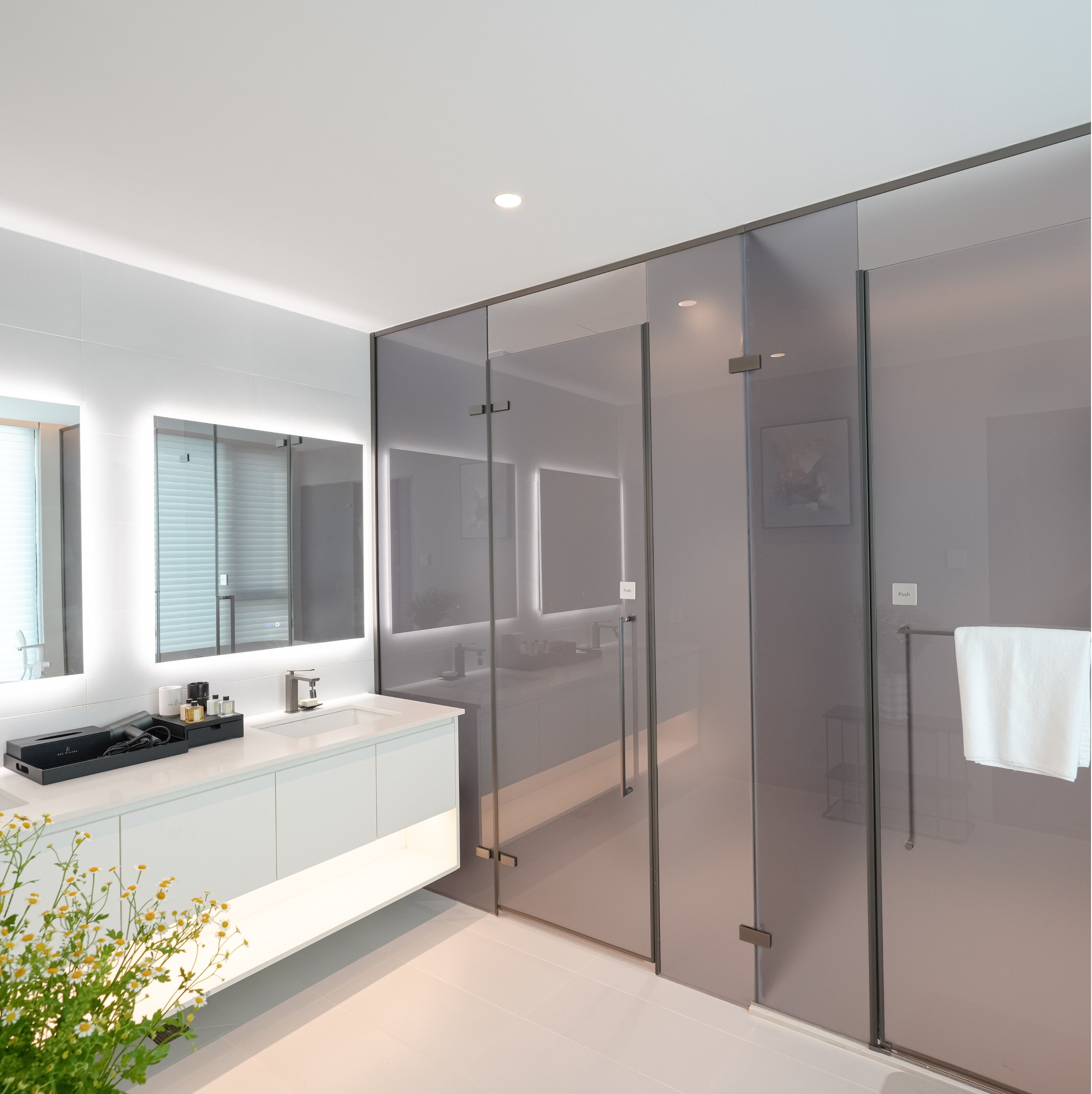 Un baño moderno con cabina de ducha de vidrio, tocador blanco y un espejo grande.