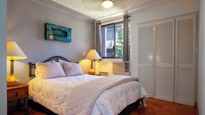 Een slaapkamer met een bed, twee bedlampen, een nachtkastje, een raam met gordijnen en een kledingkast.