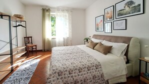 Une chambre à coucher comprenant un lit, une chaise, un radiateur, une fenêtre avec des rideaux et des tableaux encadrés accrochés au mur.