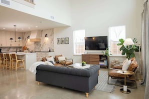 A modern living room with a sofa, chairs, a TV, and a dining area with a kitchen in the background.