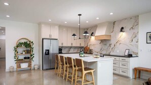 A modern kitchen with white cabinets, a marble backsplash, and a central island with bar stools.