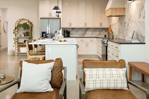 A modern kitchen with white cabinets, a marble backsplash, and a central island with seating.