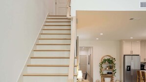 A staircase leading to a second floor, a kitchen area with a refrigerator, and a dining area with chairs.