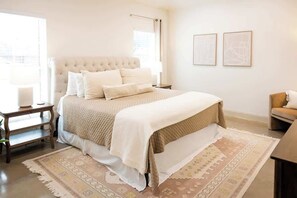 A bedroom with a large bed, a bedside table, a chair, and two framed pictures on the wall.