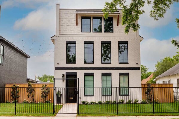 A modern two-story house with a flat roof, large windows, and a well-maintained lawn.