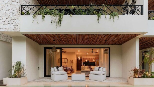A modern outdoor living area with a pool, two white sofas, and a dining table.
