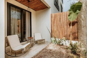 A patio with two wicker chairs, a small round table, and a bamboo fence.