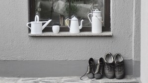 A window sill with white ceramic teapots, a cup, and a plant. Below, there are two pairs of shoes.