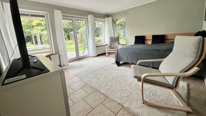 A bedroom with a bed, a chair, a desk with a computer, and a view of the outdoors.