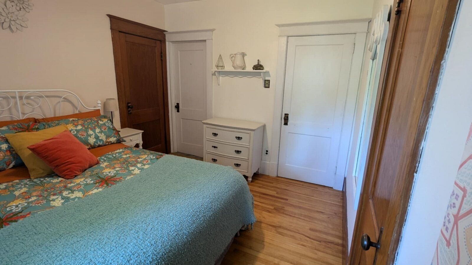 A bedroom with a bed, a nightstand, a dresser, and two doors.