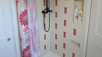 A shower area with a white tiled wall, a showerhead, and a shelf with toiletries.