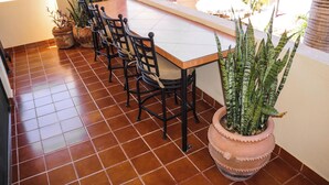Un espace repas avec une longue table et quatre chaises, entouré de plantes en pot.