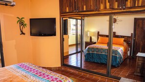 Une chambre d’hôtel avec un grand lit, une télévision, une porte-fenêtre coulissante donnant sur un balcon et un plafond en bois.