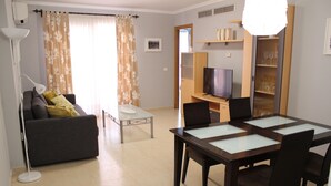 A living room with a sofa, a coffee table, a TV, and a dining area with a glass-top table and chairs. - Apartamento CON Gran Terraza Y Acceso Directo A Piscina (Dénia)