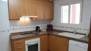 A kitchen with wooden cabinets, a built-in oven, a dishwasher, and a window with blinds. - Apartamento CON Gran Terraza Y Acceso Directo A Piscina (Dénia)