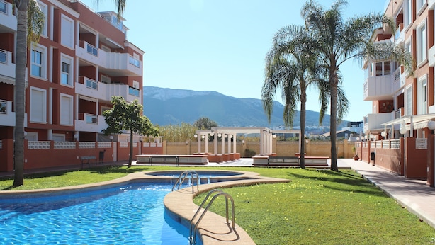 A swimming pool with a curved edge, surrounded by a well-maintained lawn and palm trees. - Apartamento CON Gran Terraza Y Acceso Directo A Piscina (Dénia)
