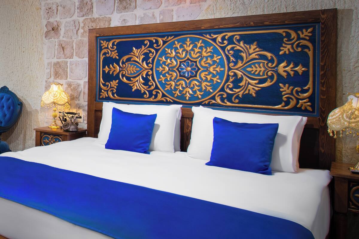A bed with a blue and white bedspread, two blue pillows, and a decorative headboard with a blue and gold pattern.