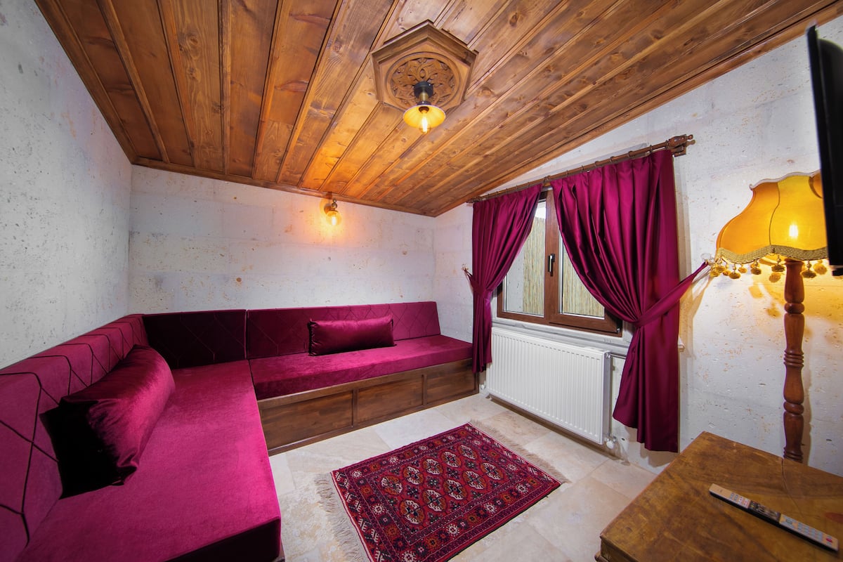 A cozy room with a wooden ceiling, a red sofa, a patterned rug, and a lamp.