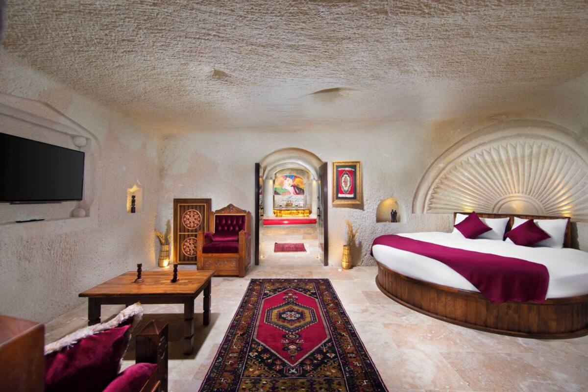 A room with a large bed, a wooden table, a sofa, and a TV.
