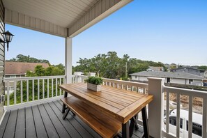 Een houten terras met een tafel en bank, met uitzicht op een woonwijk met huizen en bomen.