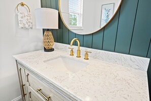 Een badkamer met een witte marmeren wastafel, gouden kraanwerk en een ronde spiegel met een gouden lijst.
