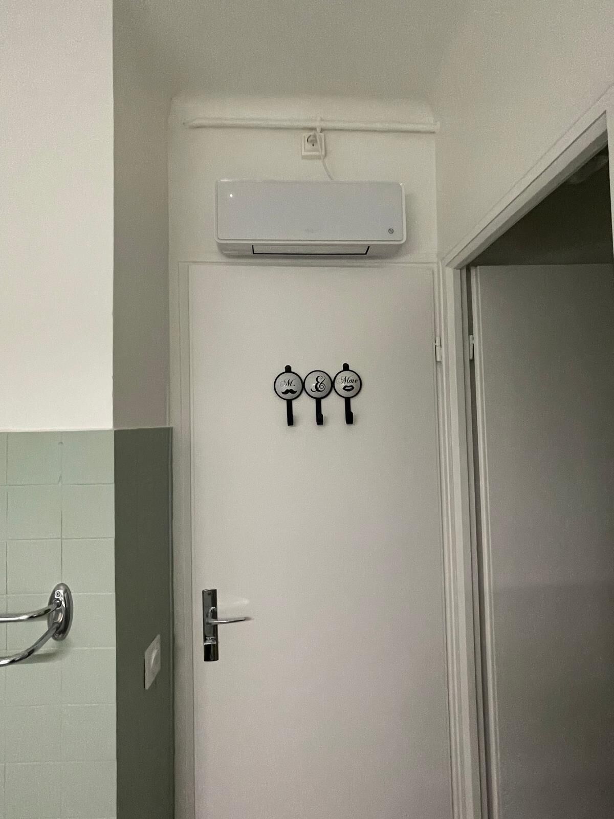 Een badkamer met een witte deur, een handdoekhouder met drie haken en een wandairconditioning.