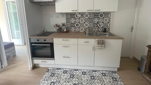 A compact kitchen with white cabinets, a patterned backsplash, a sink, and a stove. - Mise au Vert F2 à 5 mns des Commerces et 2 mns des Thermes Mer et la Montage (Amélie-les-Bains-Palalda)