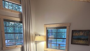 A modern living room with a grey sofa, a wooden dining table, and two windows with curtains.