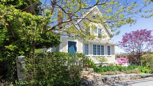 A two-story house with a blue door, surrounded by lush greenery and flowering plants. - Plum Cove Beach Paradise. Overlook Plum Cove from your kitchen n only steps away (Gloucester)