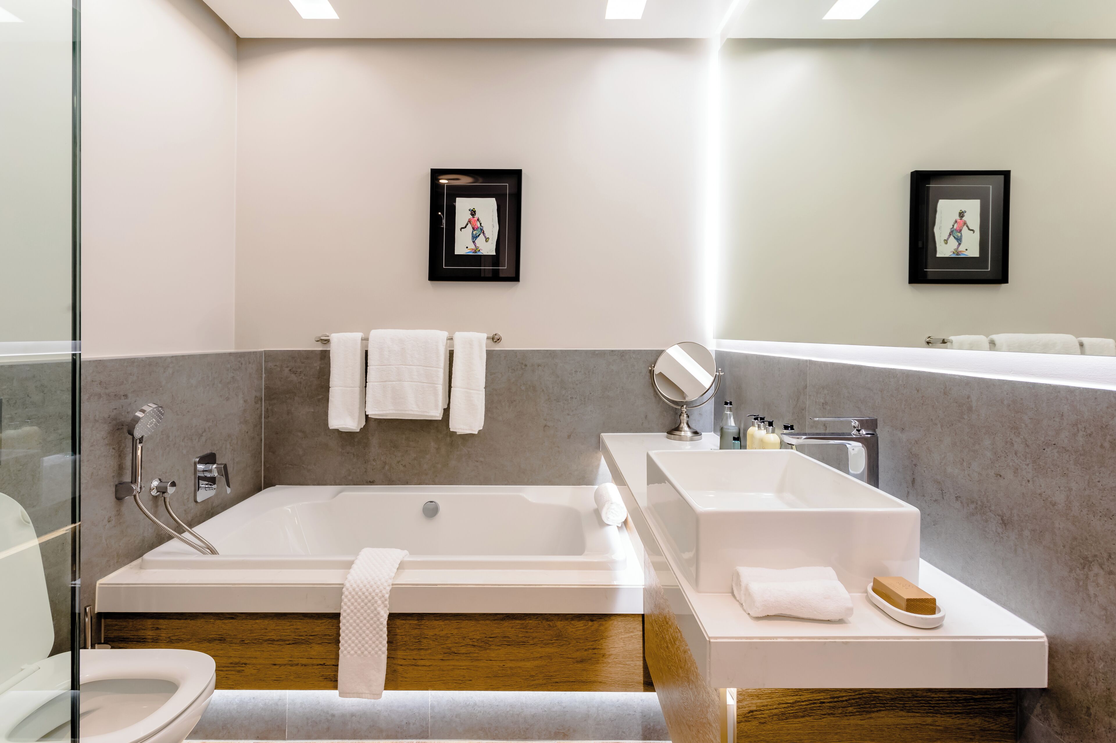 Um banheiro moderno com banheira, pia e vaso sanitário. Há duas fotos emolduradas na parede, um porta-toalhas e um espelho.