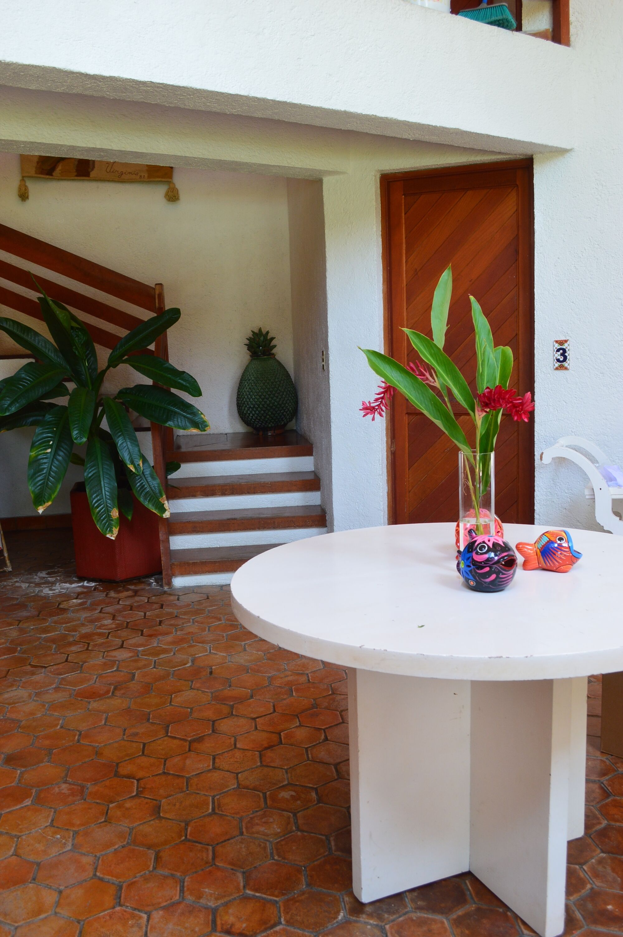 A white table with a vase of flowers and a decorative fish, a potted plant, and a staircase leading to a wooden door.