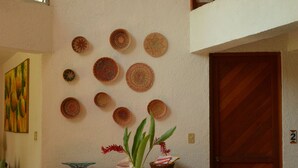 Une pièce avec une table ronde, un luminaire suspendu en fibres tressées et un mur décoré d’assiettes en fibres tressées.