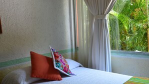 Un lit avec une literie blanche, un coussin à motifs floraux colorés et une couverture à rayures.