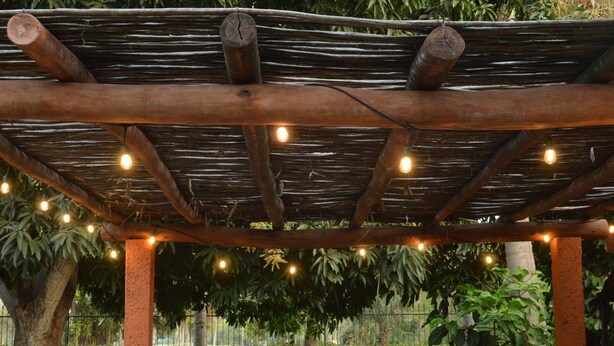 Une pergola en bois, décorée de guirlandes lumineuses, avec un hamac et une végétation luxuriante en arrière-plan.