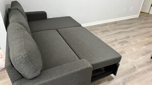A sectional sofa with a dark fabric, positioned against a plain wall with a light-colored wooden floor. - Game On! Resort -- Ask us about special weekly and monthly deals (Emerson)
