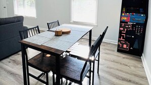 A dining area with a wooden table, chairs, a chandelier, and a pinball machine. - Game On! Resort -- Ask us about special weekly and monthly deals (Emerson)