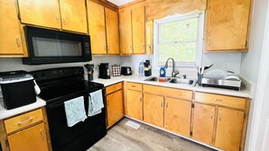 A compact kitchen with wooden cabinets, a microwave, a stove, a sink, and a window. - Game On! Resort -- Ask us about special weekly and monthly deals (Emerson)