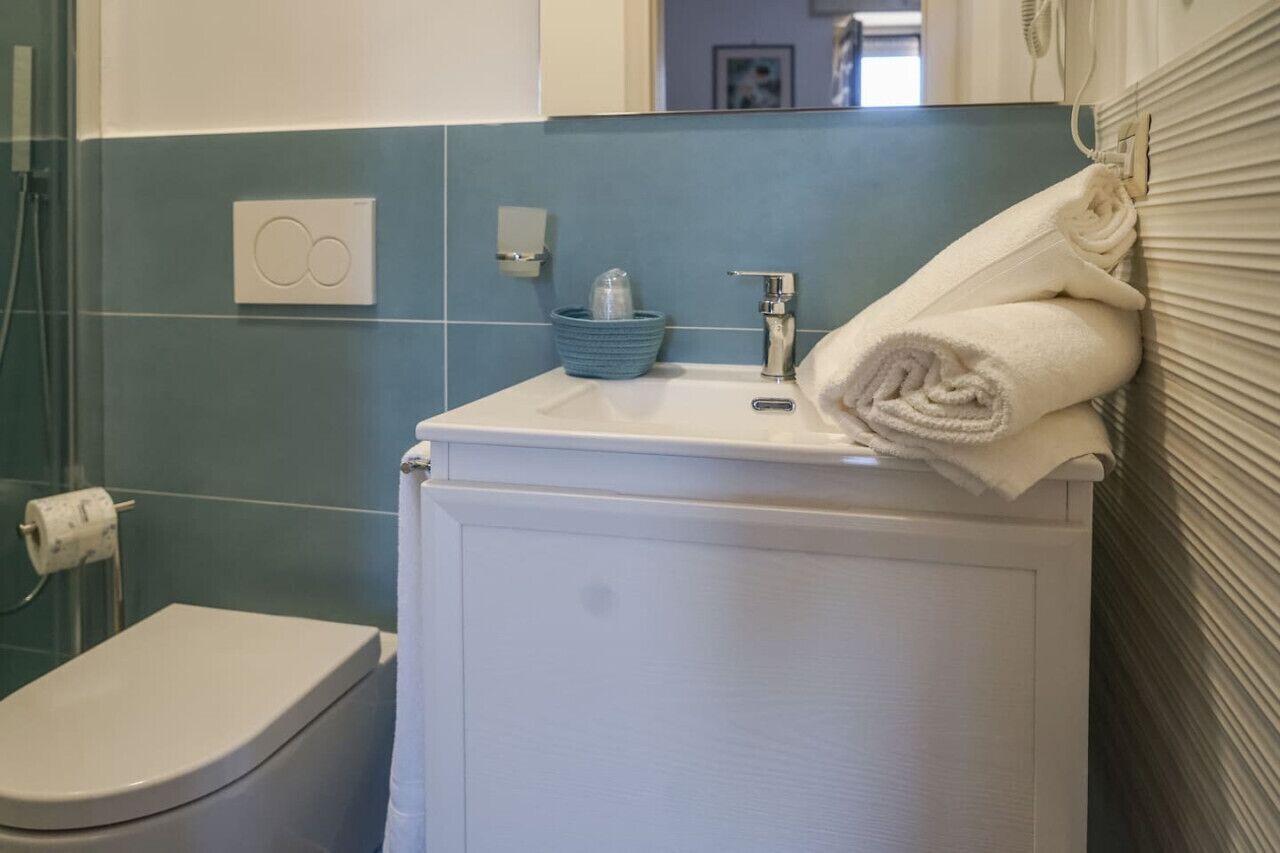 Un baño con un inodoro blanco, un lavabo con un jabonera azul y una toalla en la pared.