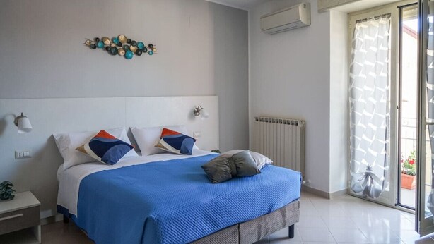 Ein Schlafzimmer mit einem großen Bett, einem Nachttisch, einer Wandleuchte, einer Heizung und Blick durch eine Glastür.
