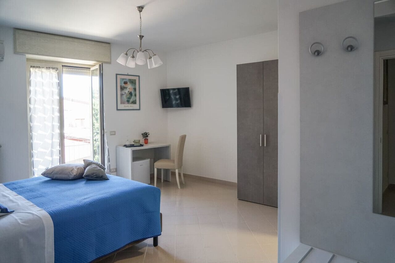 Un dormitorio con cama, escritorio, silla, armario y televisor en la pared.